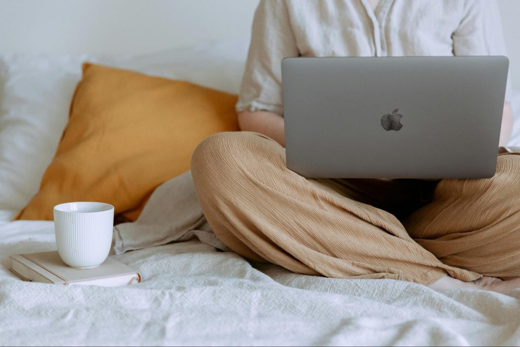 A person sitting cross-legged on a bed with a laptop on their lap, working comfortably. This image illustrates the concept of working from home and managing multiple income streams as a self-employed individual.