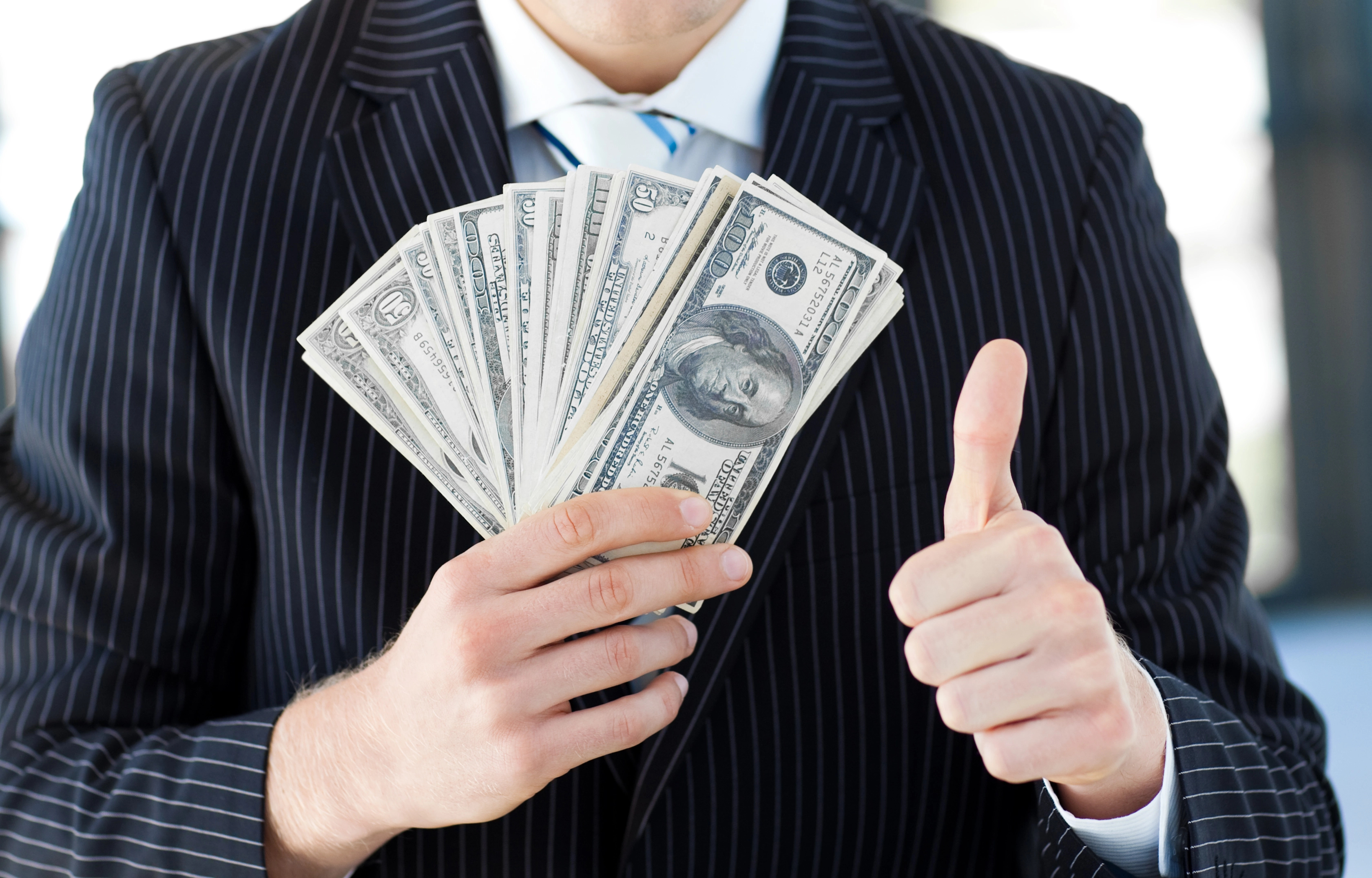A man in a suite holding cash on one hand