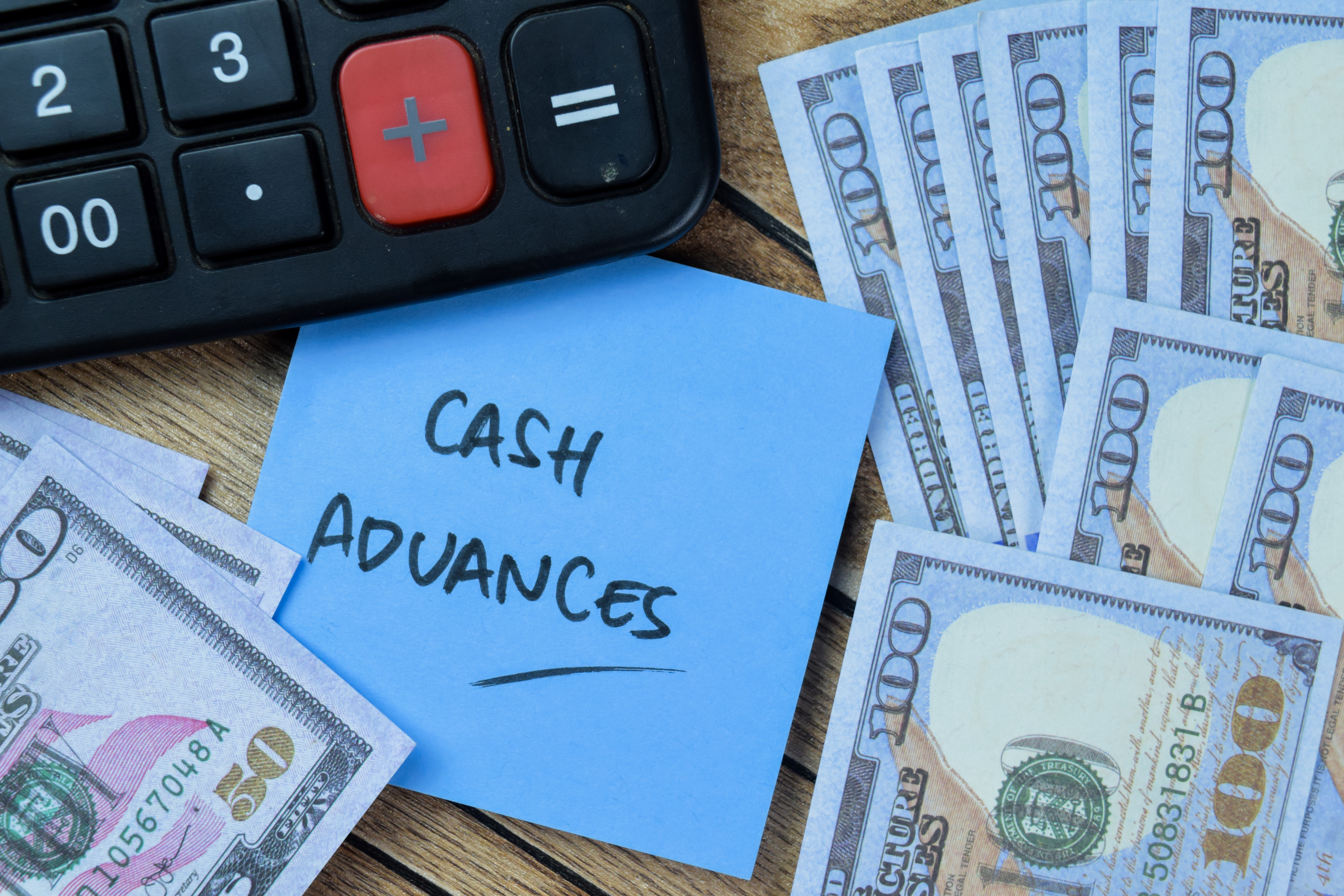 An image of a calculator, 100 and 50 dollar bills and a sticky note that has written cash advances on it.