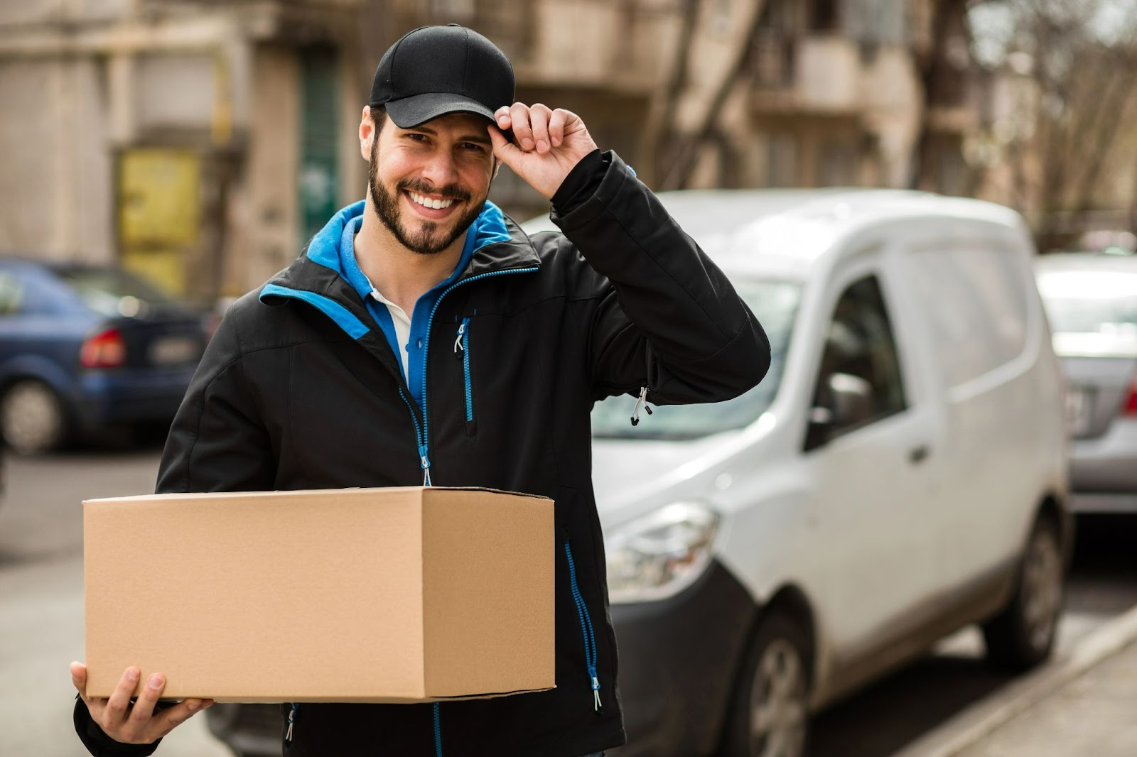 Smiling delivery man holding a cardboard box in front of a van.
