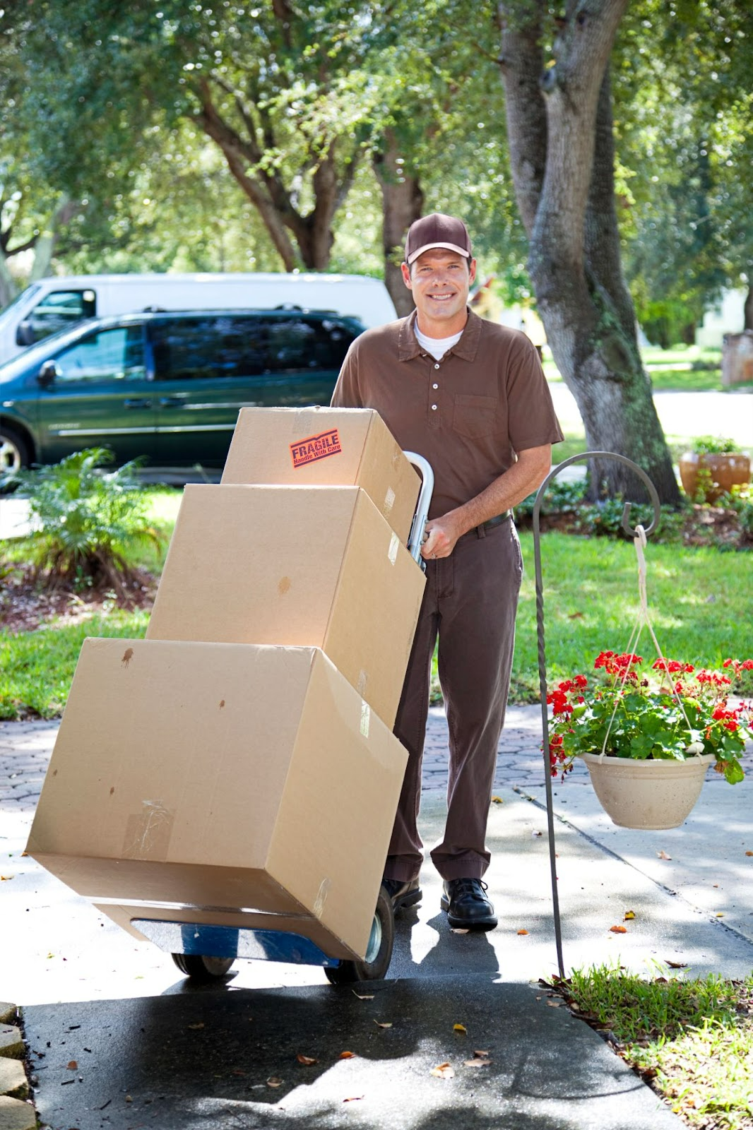 Smiling delivery man in uniform pushing a hand truck with large boxes outside a house