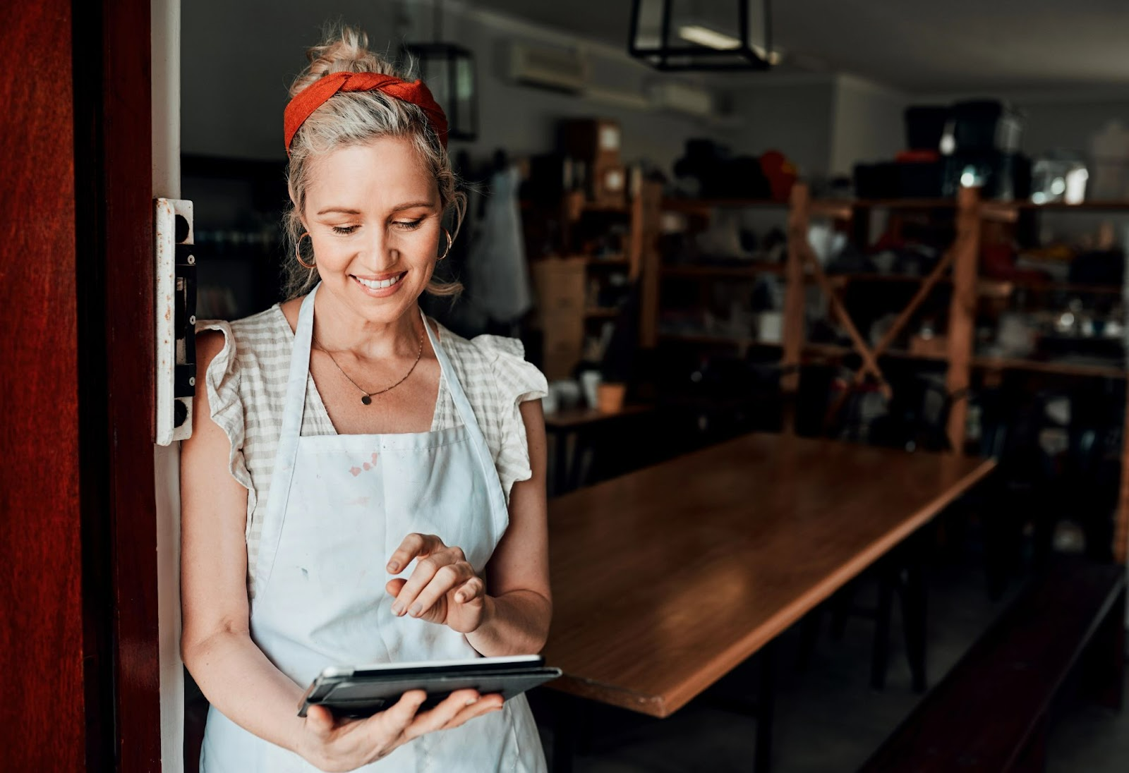 Smiling woman in an apron using a tablet inside a workshop or studio..jpg