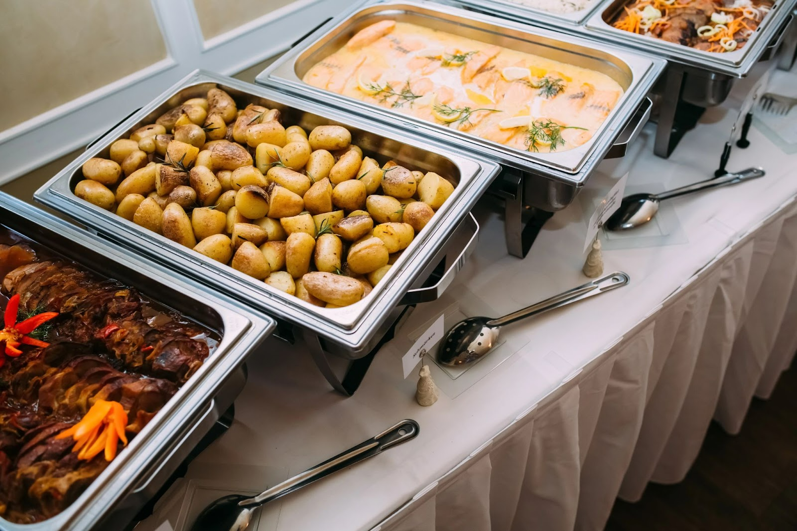 Buffet table with trays of roasted potatoes, fish in sauce, and meat dishes..jpg