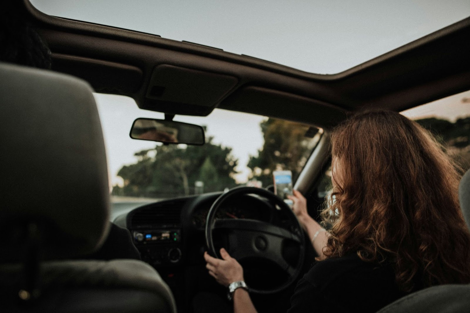 Rideshare driver holding a phone while driving a car, viewed from the back seat