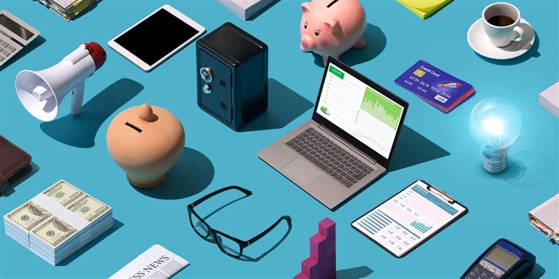 ALT text: Business and finance workspace with laptop, cash, piggy bank, credit cards, charts, and office tools on a blue background.