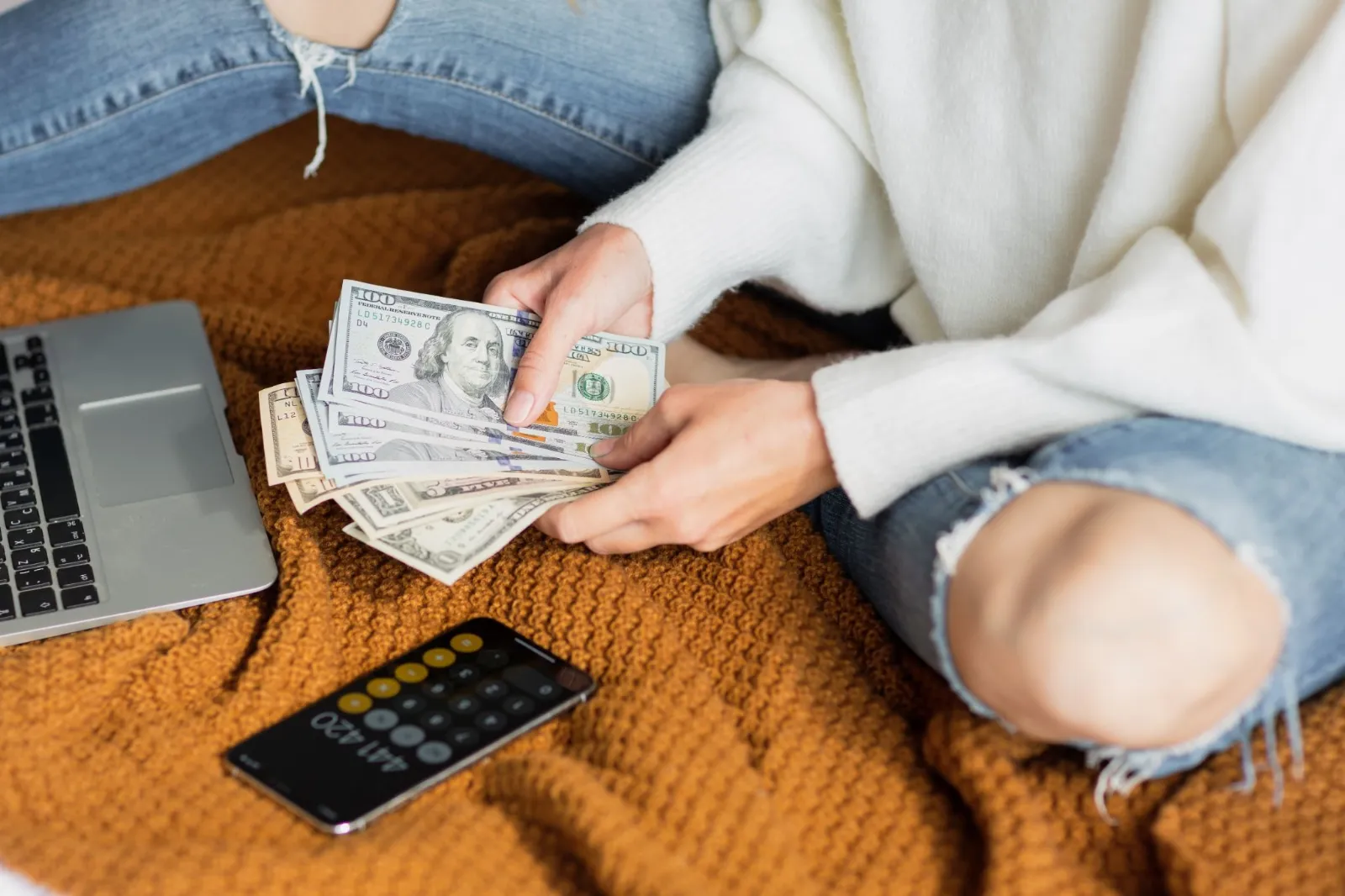 Person counting cash beside a laptop and phone calculator
