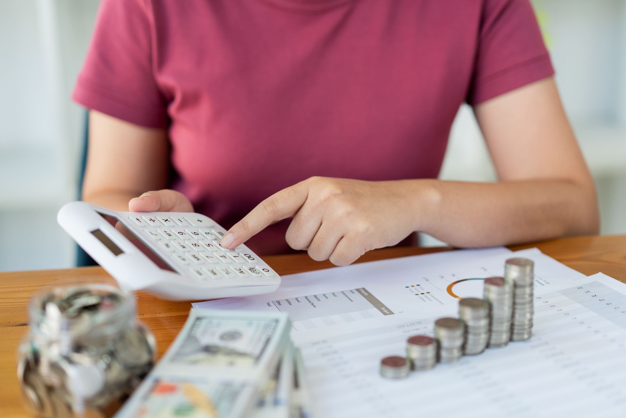 Person using a calculator with cash, coins, and financial documents on a desk.
