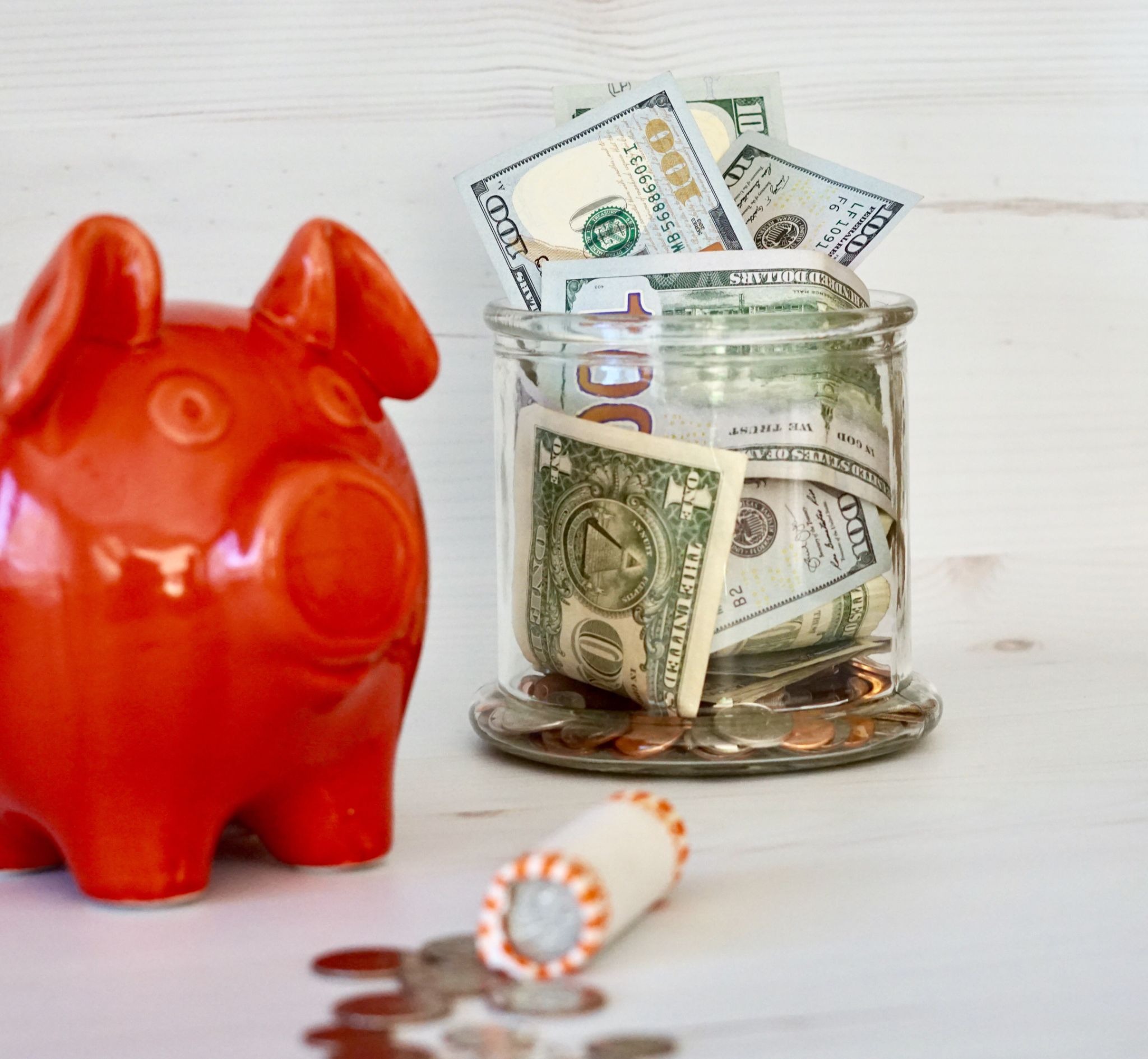 Cash and coins in a jar next to a red piggy bank