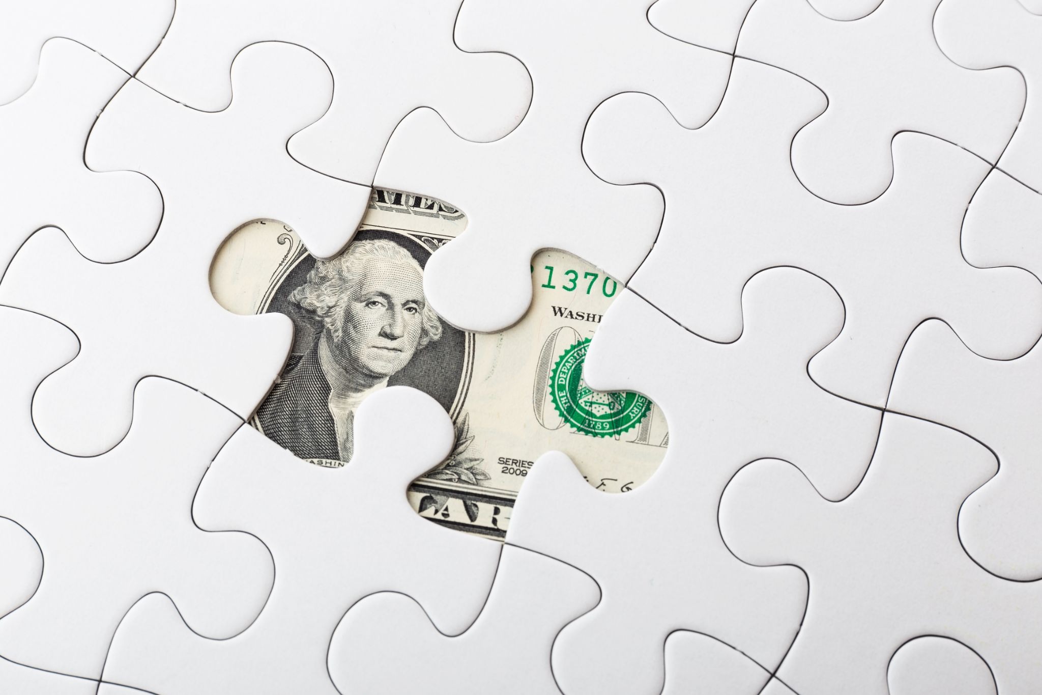 A white jigsaw puzzle with one missing piece, revealing a dollar bill underneath, symbolizing financial solutions or missing money