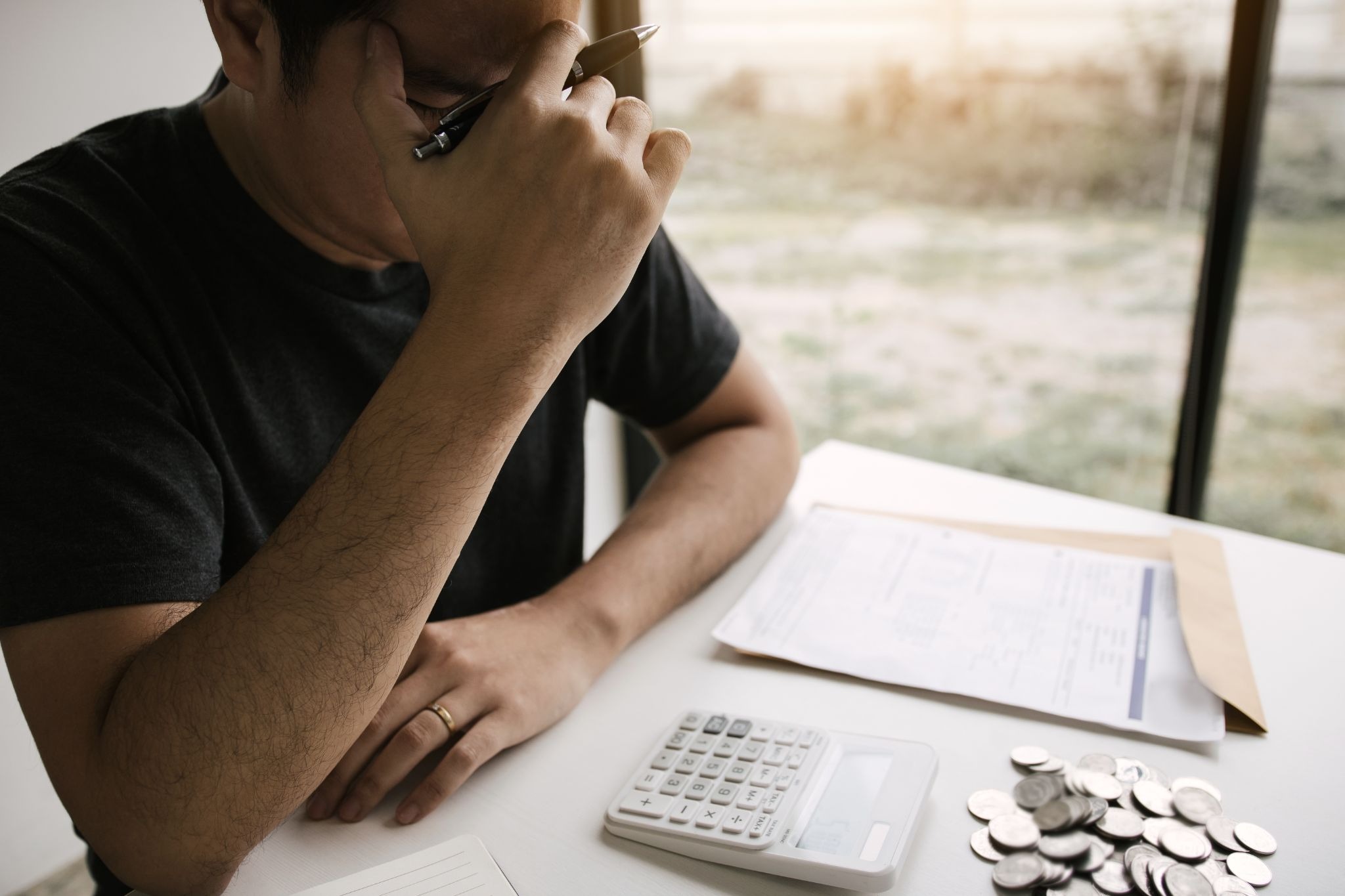 Uber driver looking stressed while reviewing bills with a calculator and coins on the table
