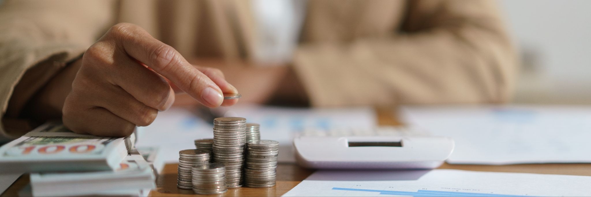 Person stacking coins on a table with cash, documents, and a calculator nearby.