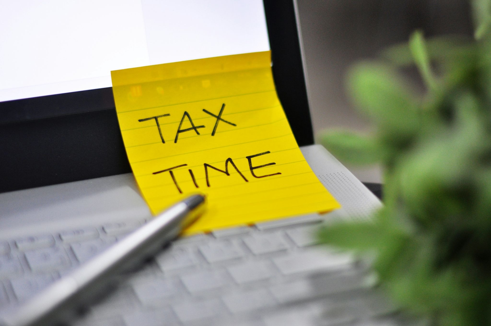 Sticky note reading “Tax Time” on a laptop keyboard with a pen