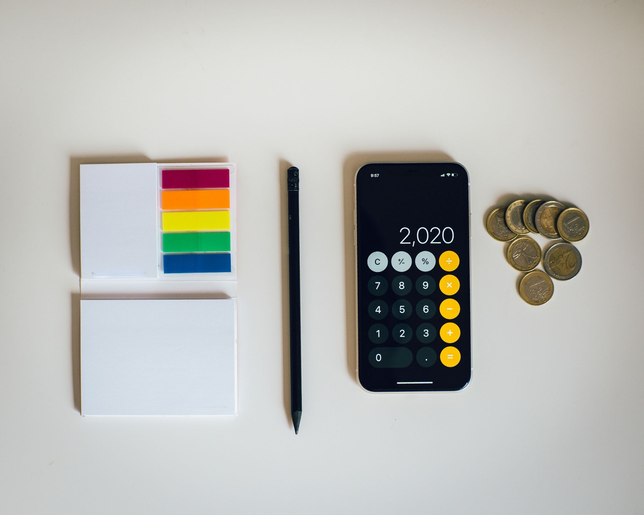 Notepad, pencil, smartphone calculator, and coins arranged on a white surface.