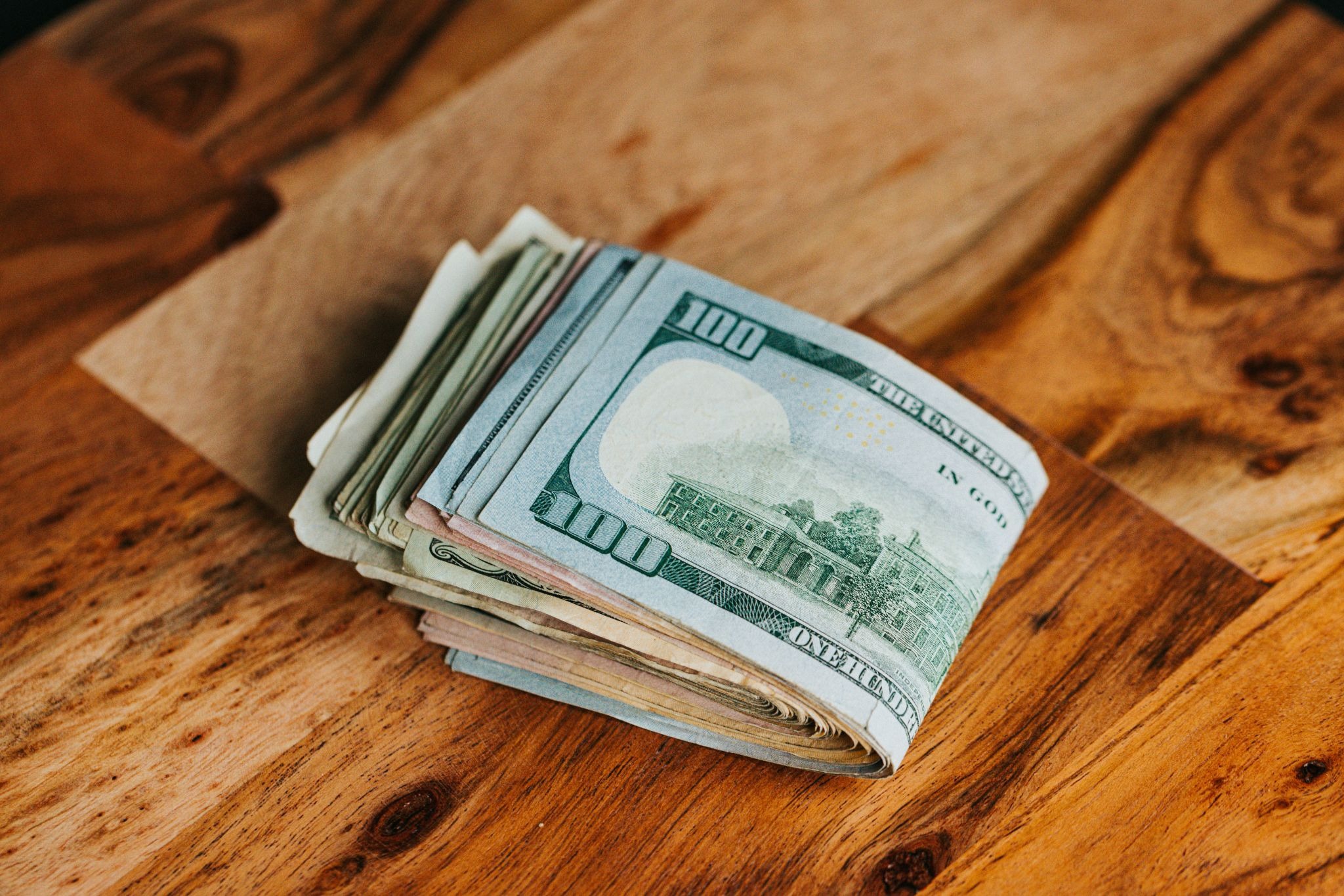 Stack of US dollar bills on a wooden table.
