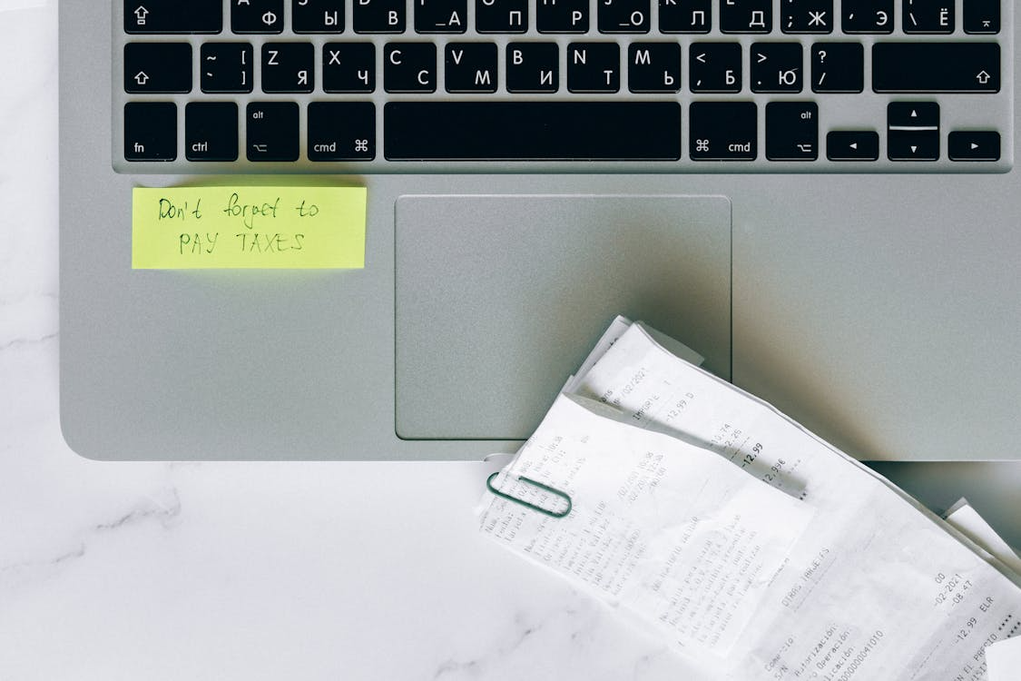 laptop with a sticky note reminding freelancer to pay taxes