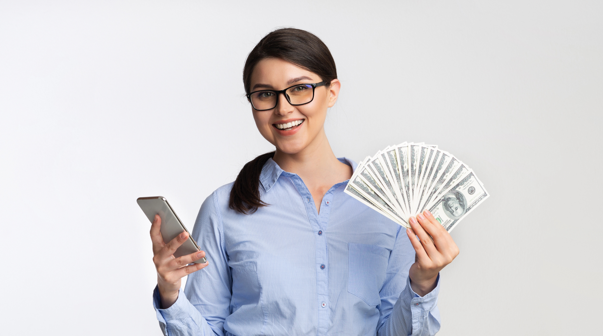 A person wearing glasses, holding a phone on one hand and cash on the other