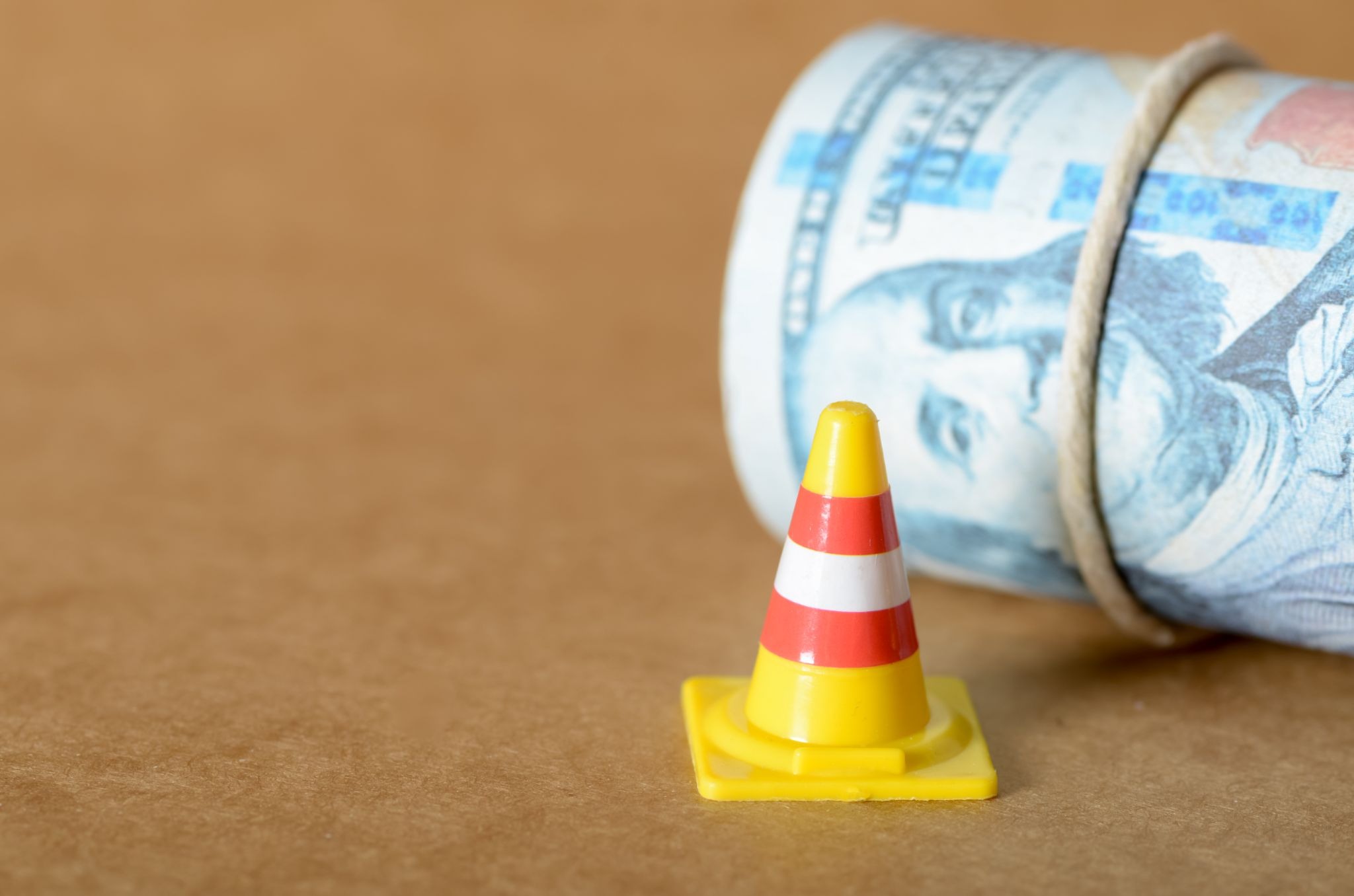 Emergency fund concept with rolled cash beside a warning cone.