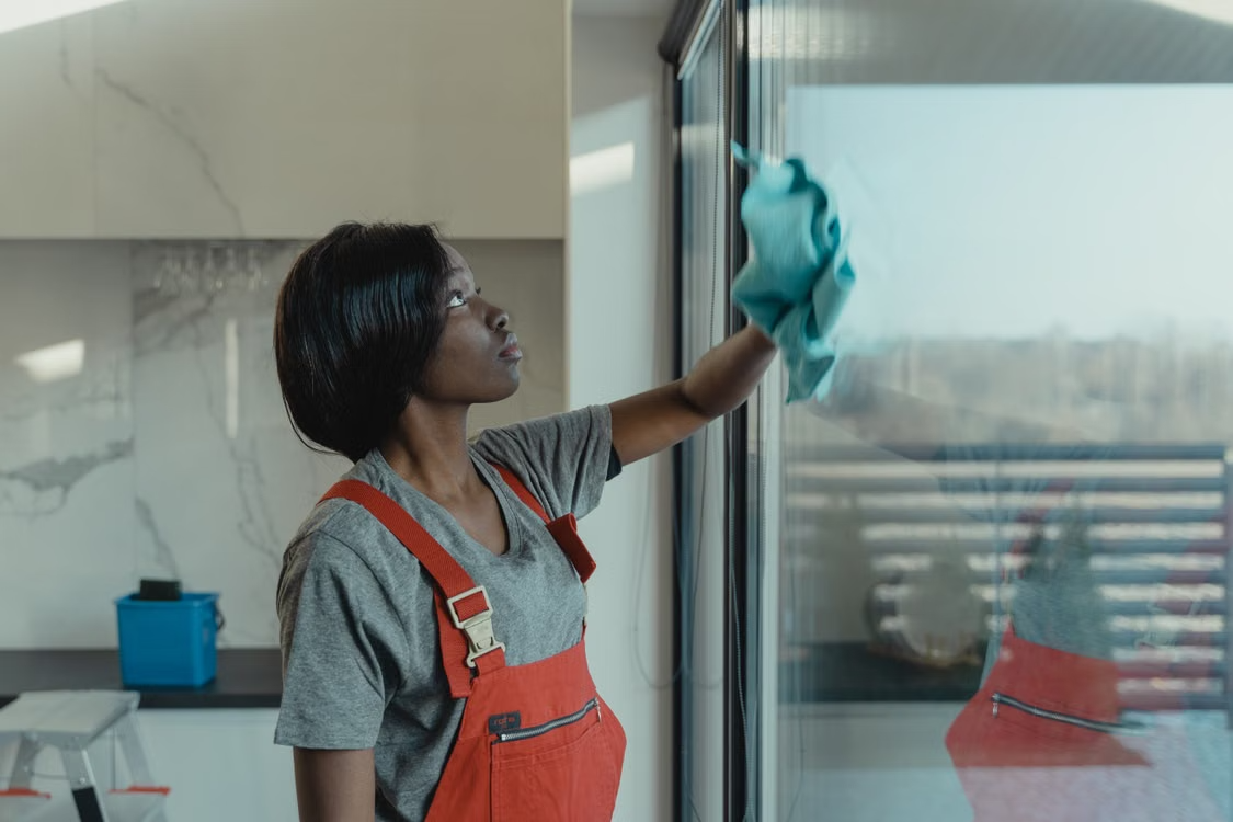 An independent cleaner wiping down a client's large windows with a cloth 