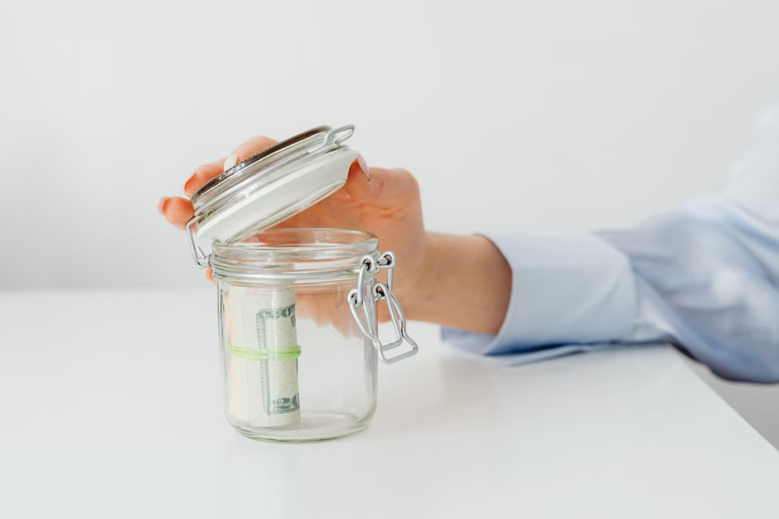 A gig worker placing money bills into a jar to build savings