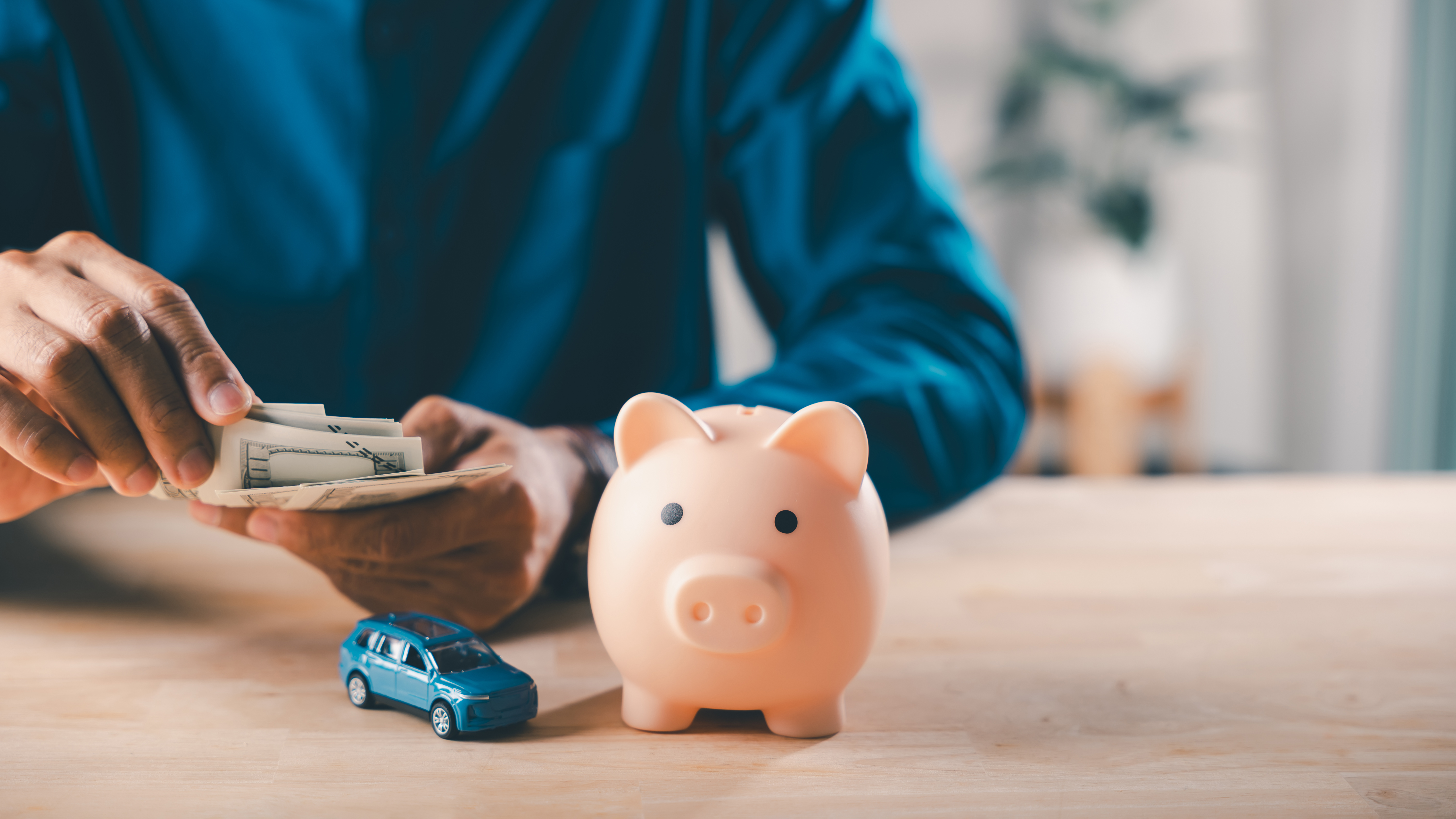 Person counting cash beside a piggy bank and toy car, representing budgeting for fixed driving expenses.