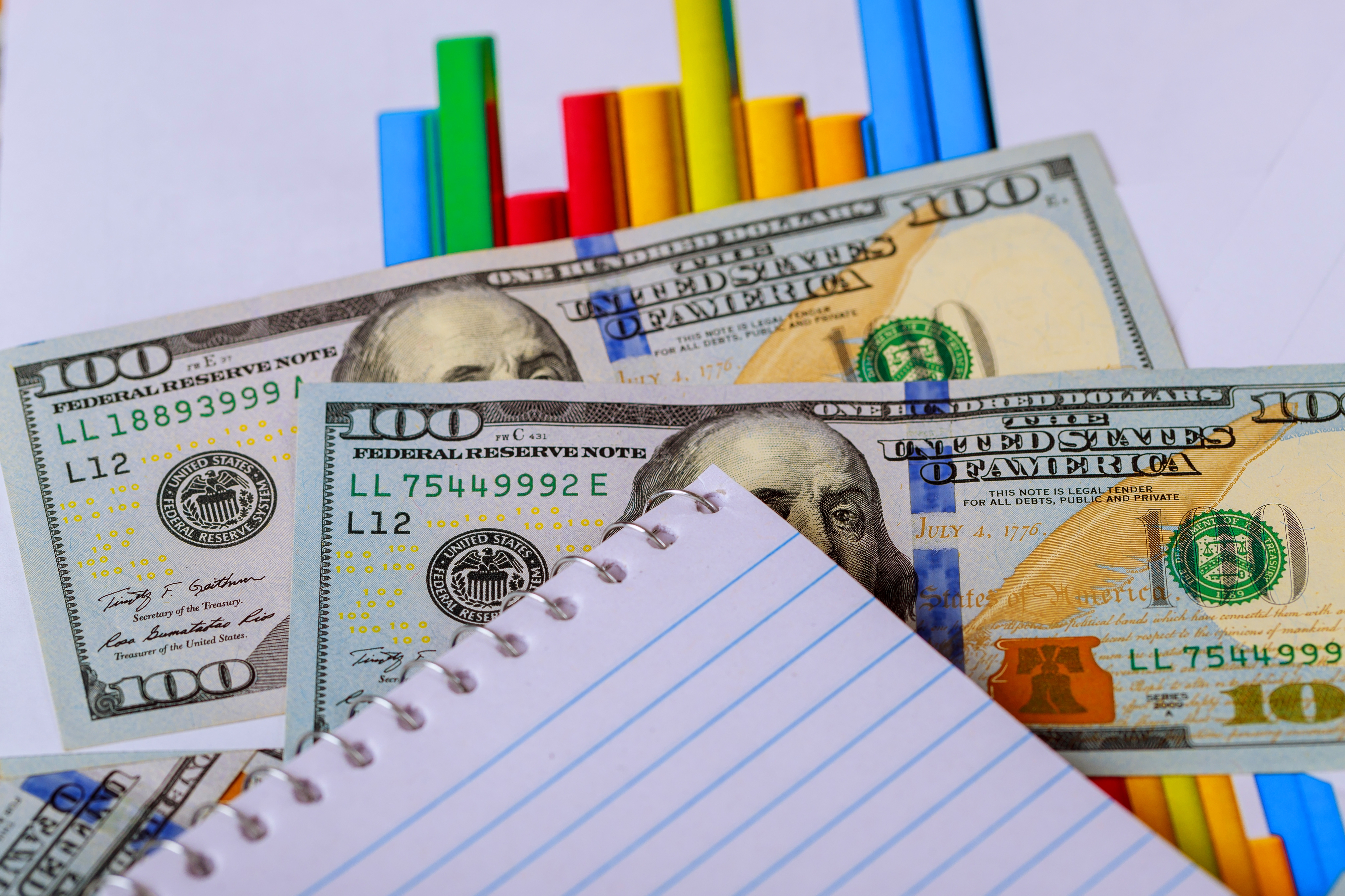 Notebook, U.S. dollar bills, and a colorful bar chart representing tutoring business expenses.