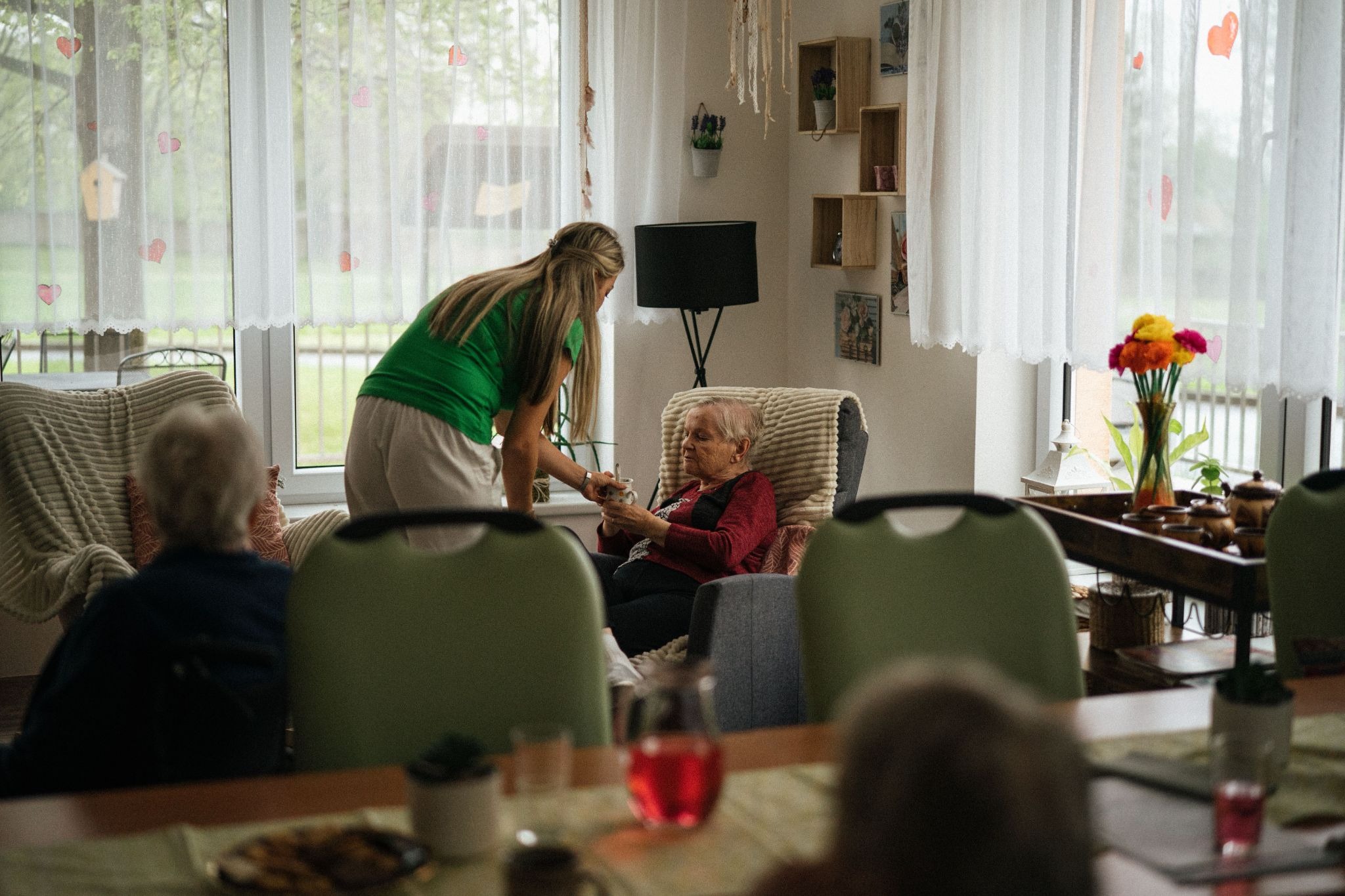 A home health aide gives a drink to their client in the client's home while providing supportive care