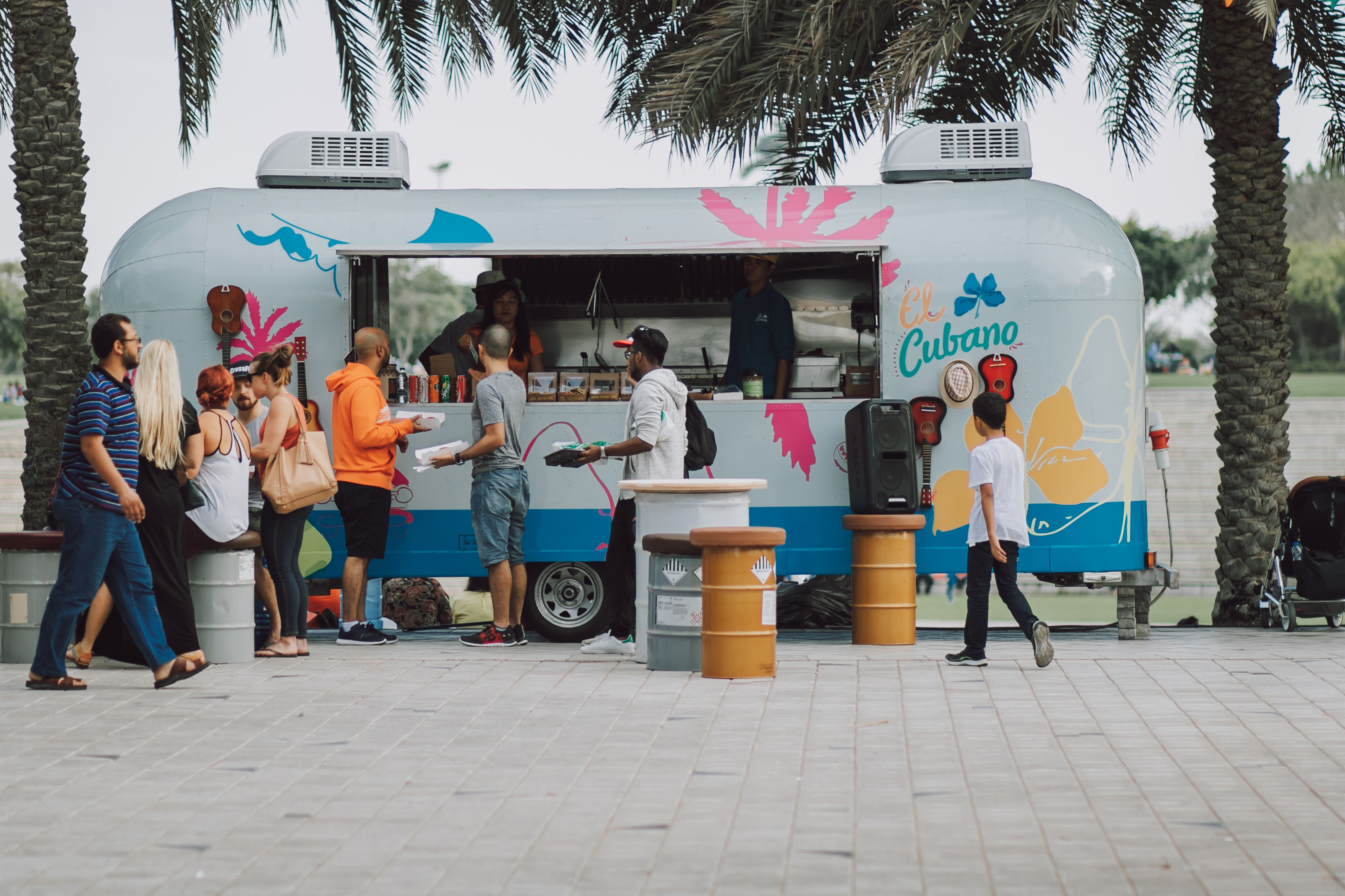 A busy food truck is parked on a city street, with a long line of customers ordering and picking up freshly prepared food.