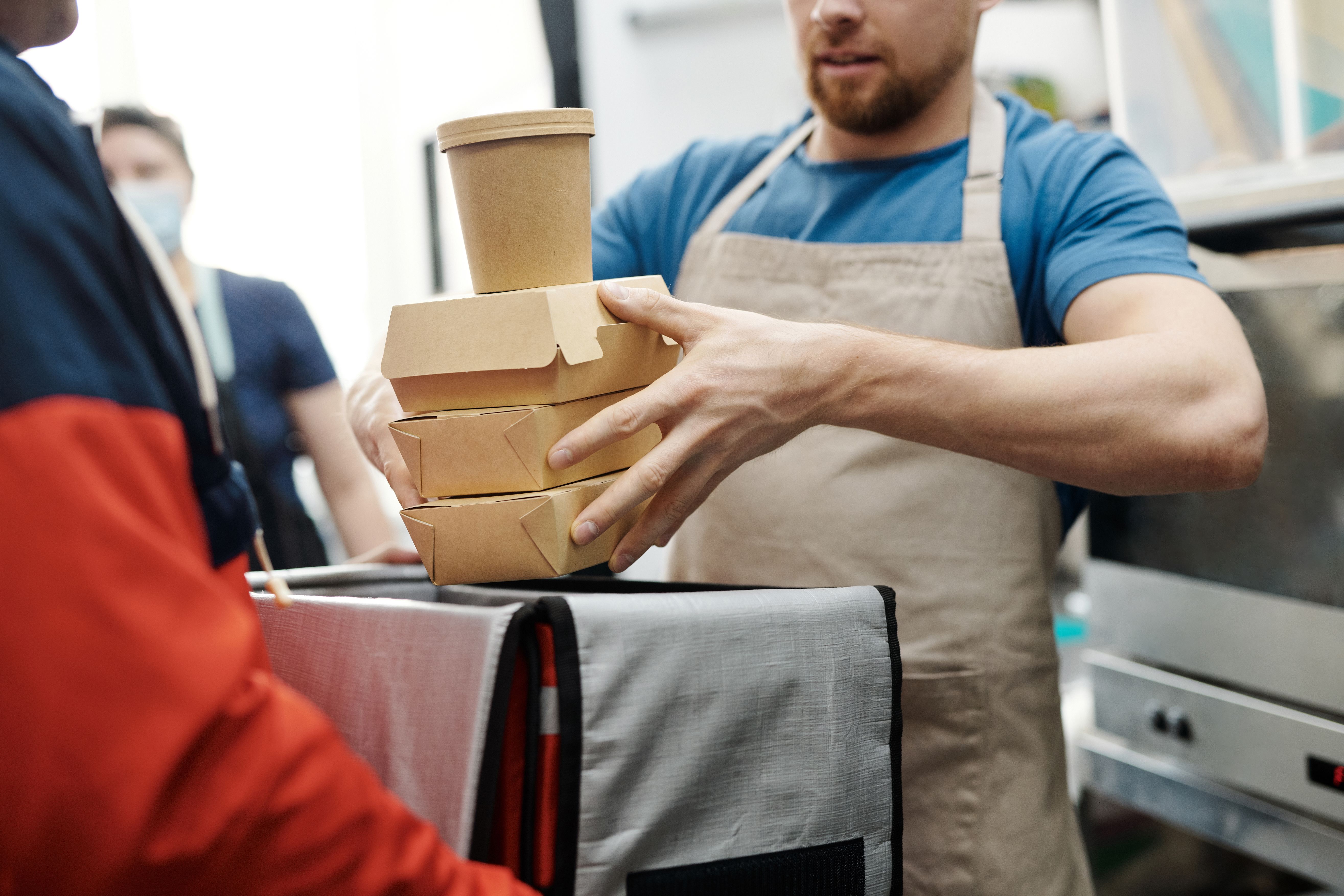 Restaurant staff placing a food order into a delivery driver's insulated delivery bag