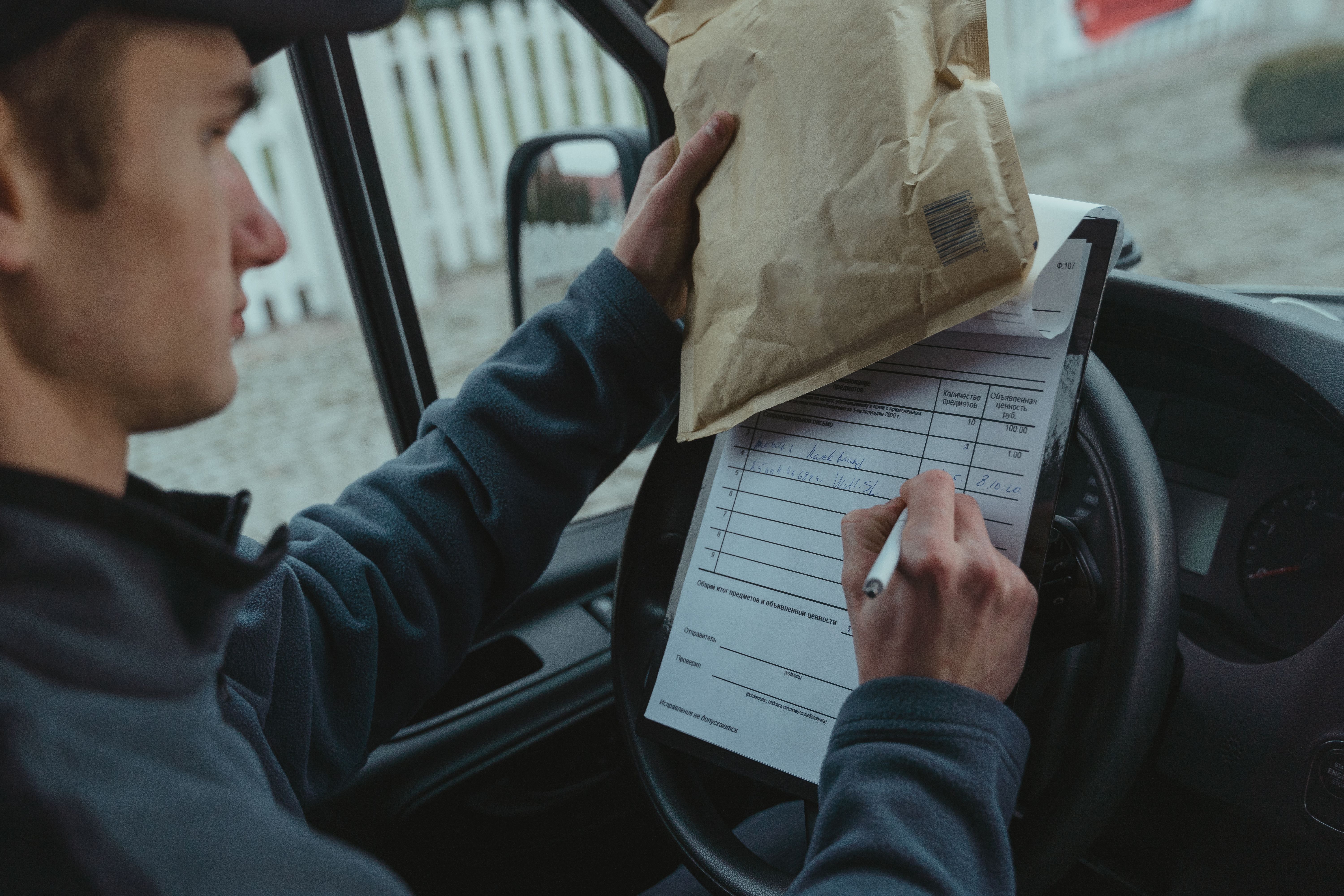 Delivery driver checking a delivery list while inside a car and holding a small package