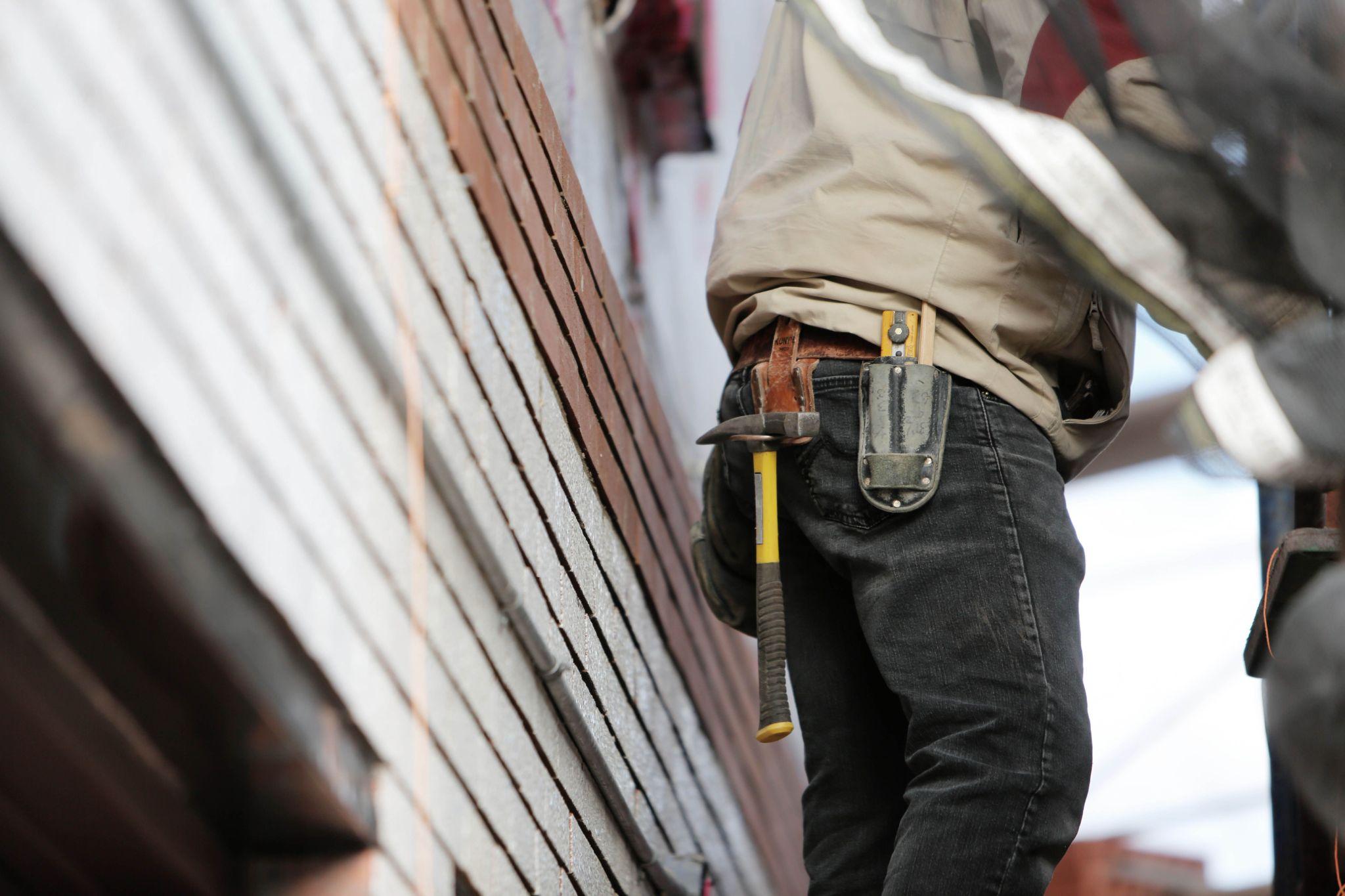 Independent handyman wearing a tool belt while completing repair work on a client’s home exterior