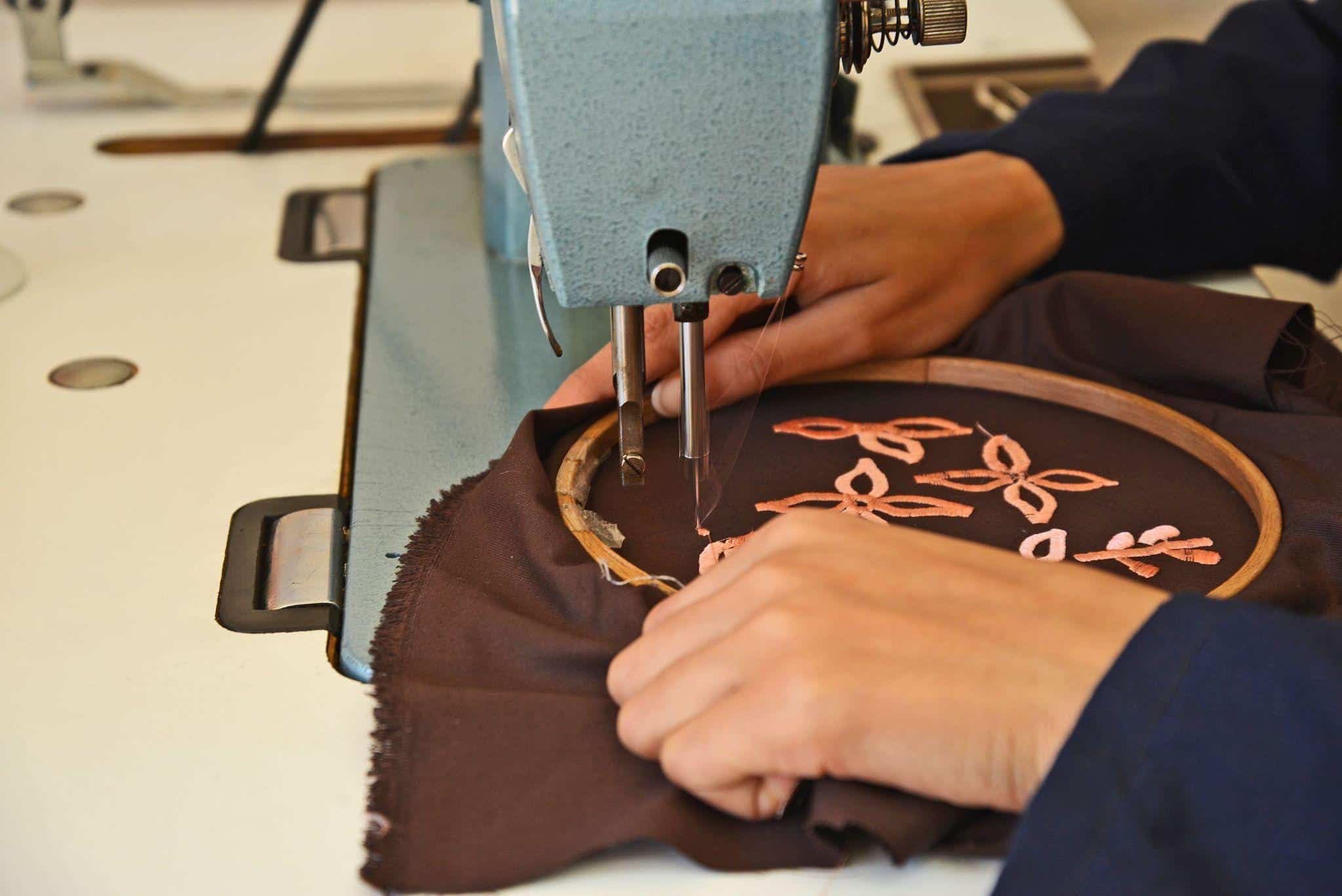 Etsy shop owner carefully embroidering a handmade order, stitching colorful thread into fabric at a worktable