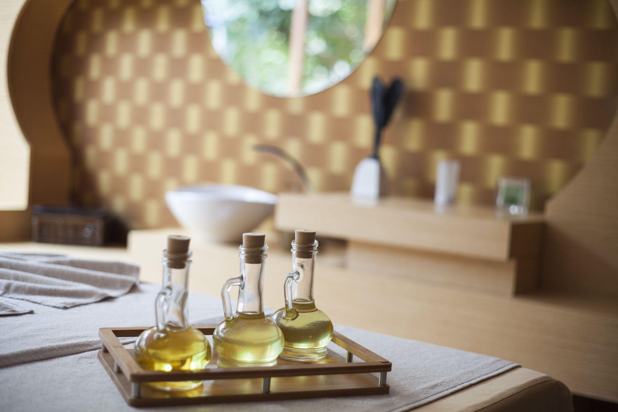 Three bottles of massage oil in different varieties arranged on a tray inside a calm massage room