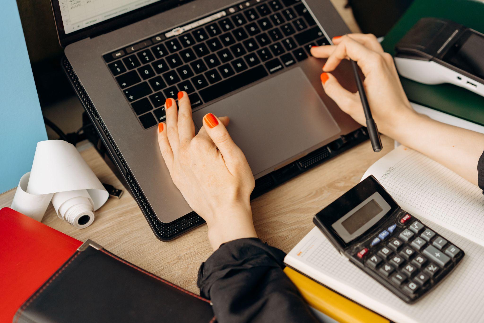 A freelance bookkeeper reviewing and organizing their client’s tax documents and financial records through their laptop and calculator