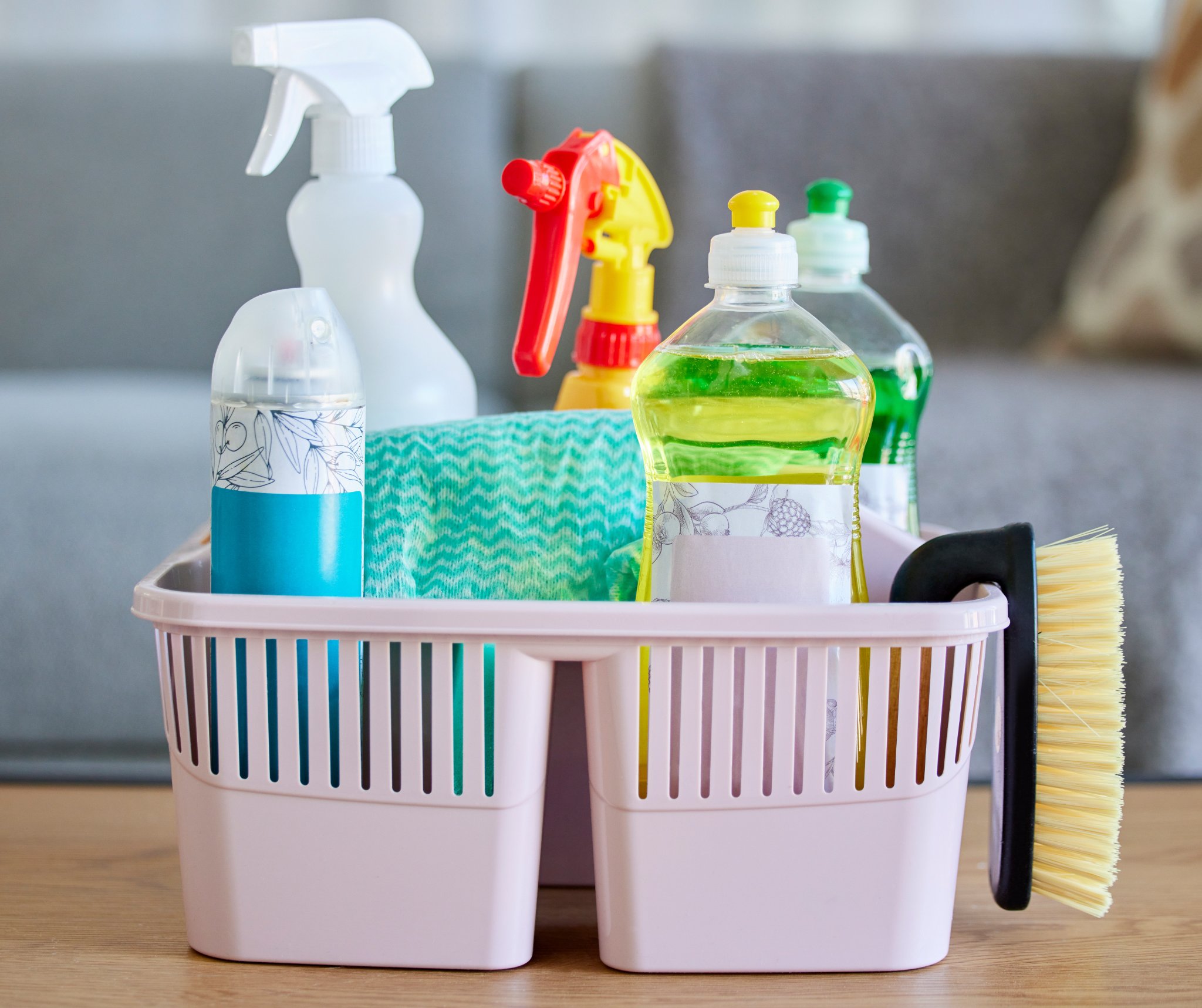 Cleaning products in a pink basket, on a table.