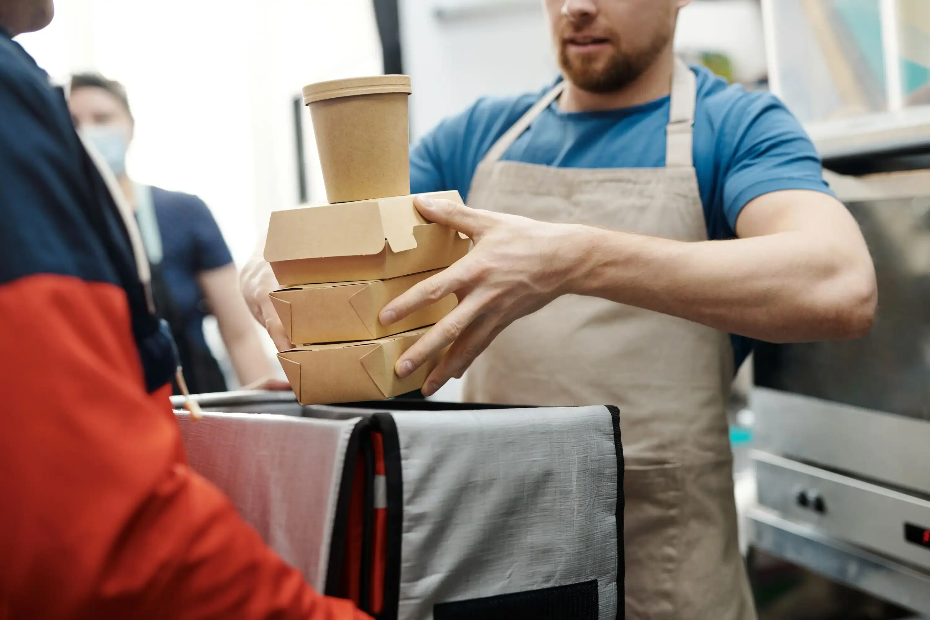 Restaurant staff placing a food order into a delivery driver's insulated delivery bag