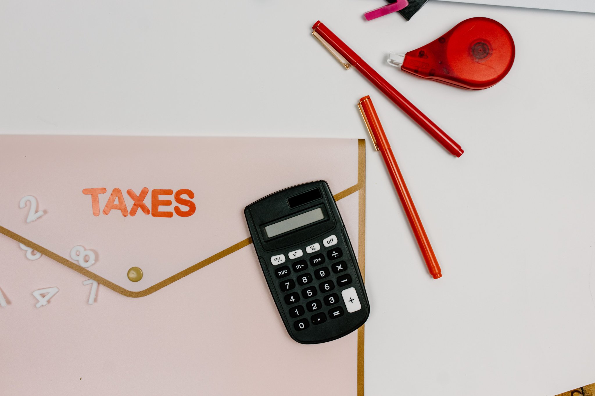 Three letter tiles spelling “TAX” sit on top of a stack of coins