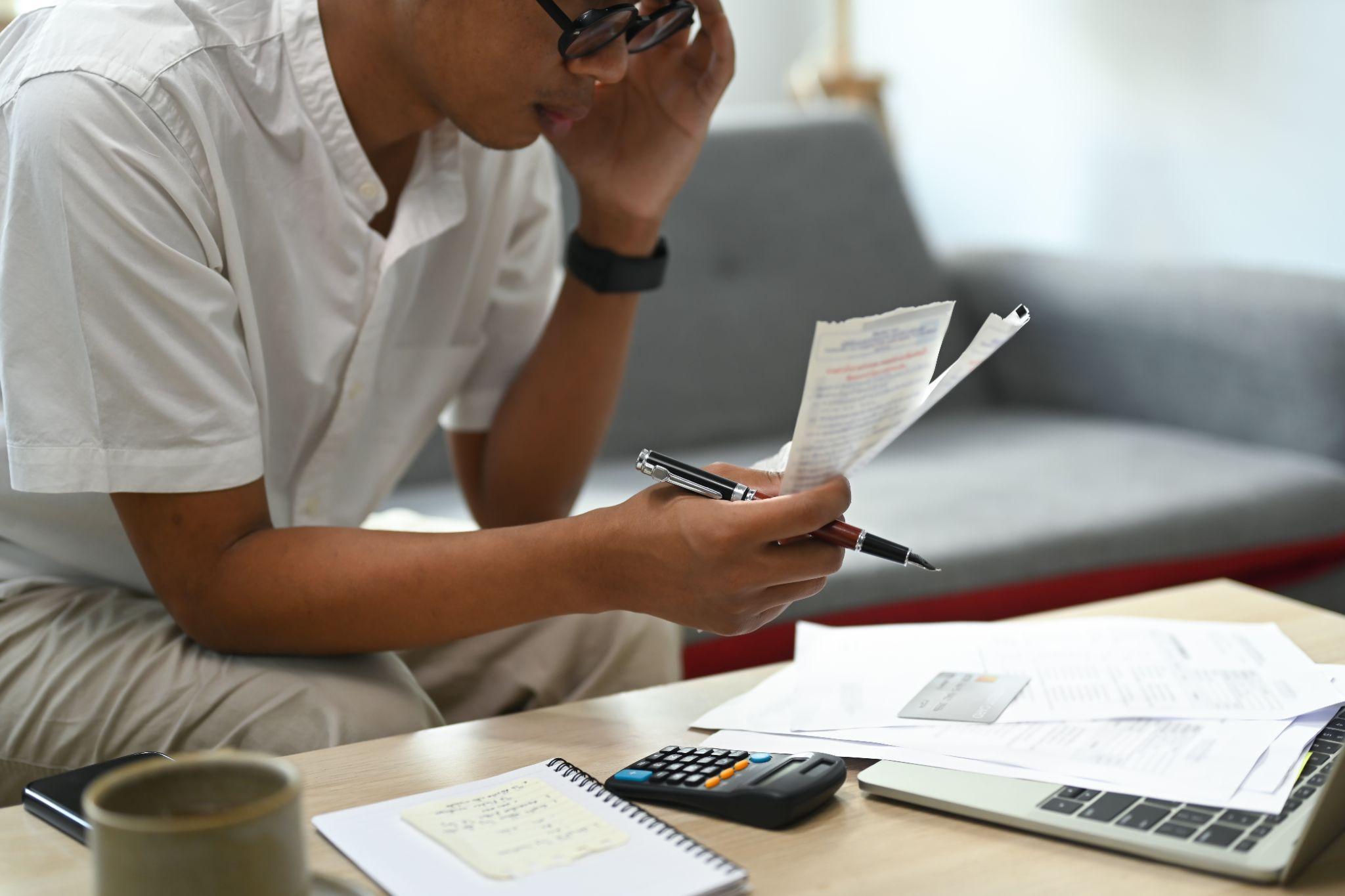 Freelancer reviewing bills and using a calculator to manage his finances.