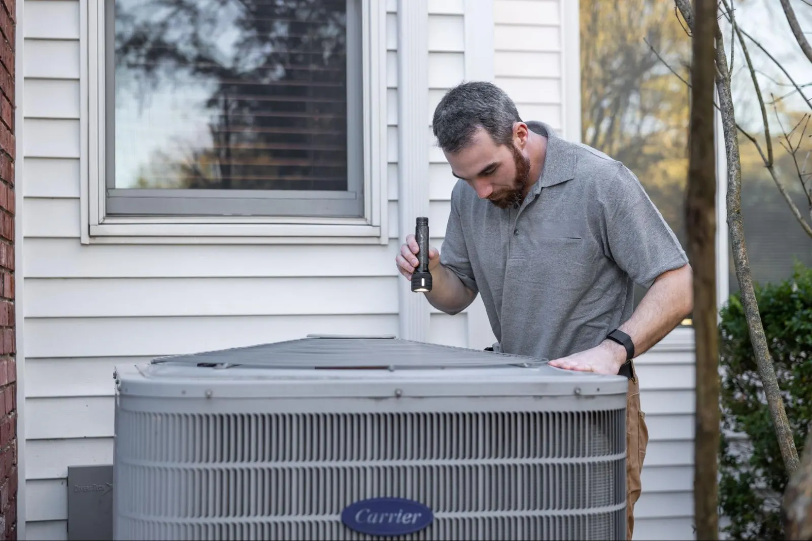 HVAC contractor outdoors using a flashlight to inspect the inside of an HVAC system