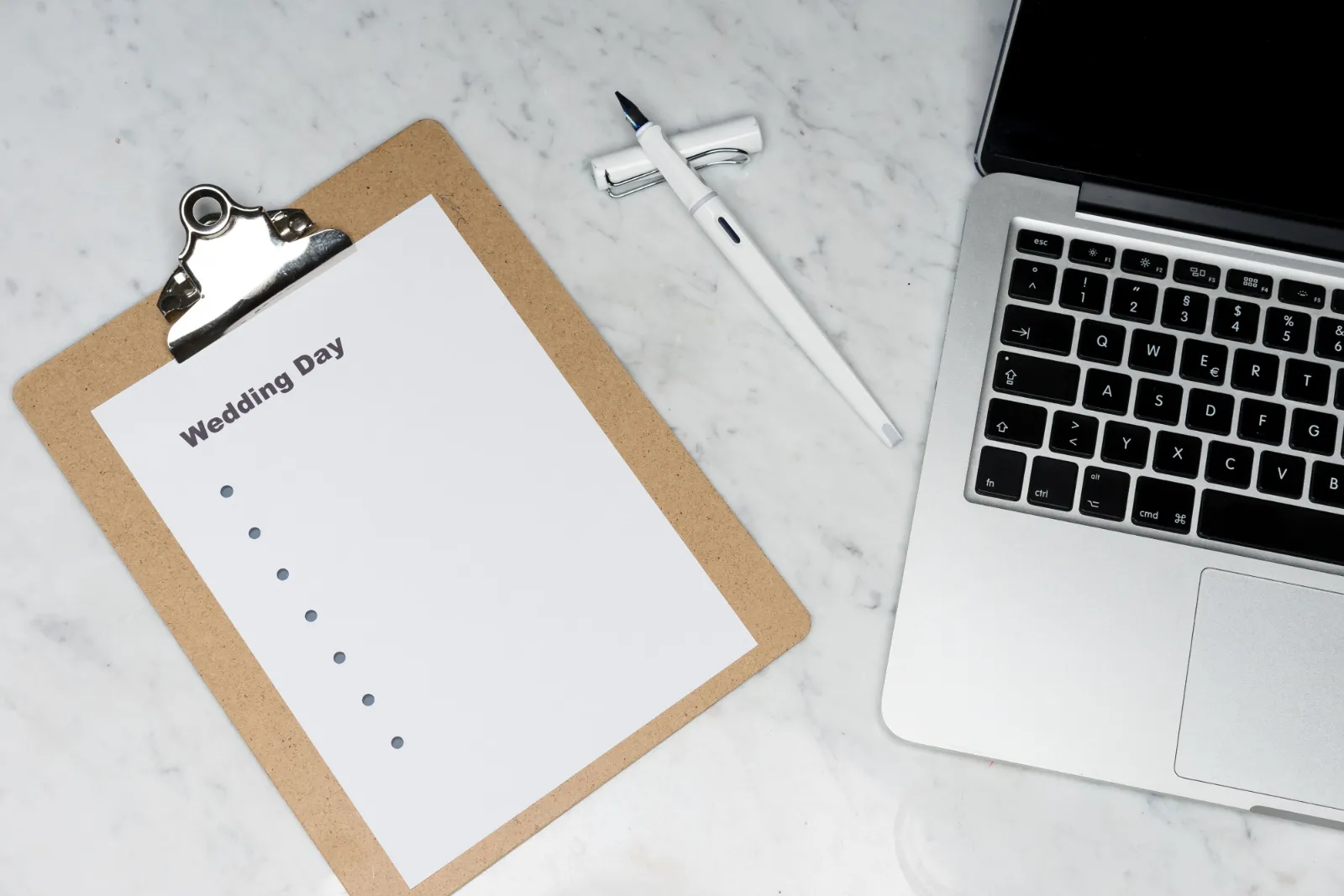 Clipboard with a blank wedding day checklist beside a fountain pen and laptop on a table